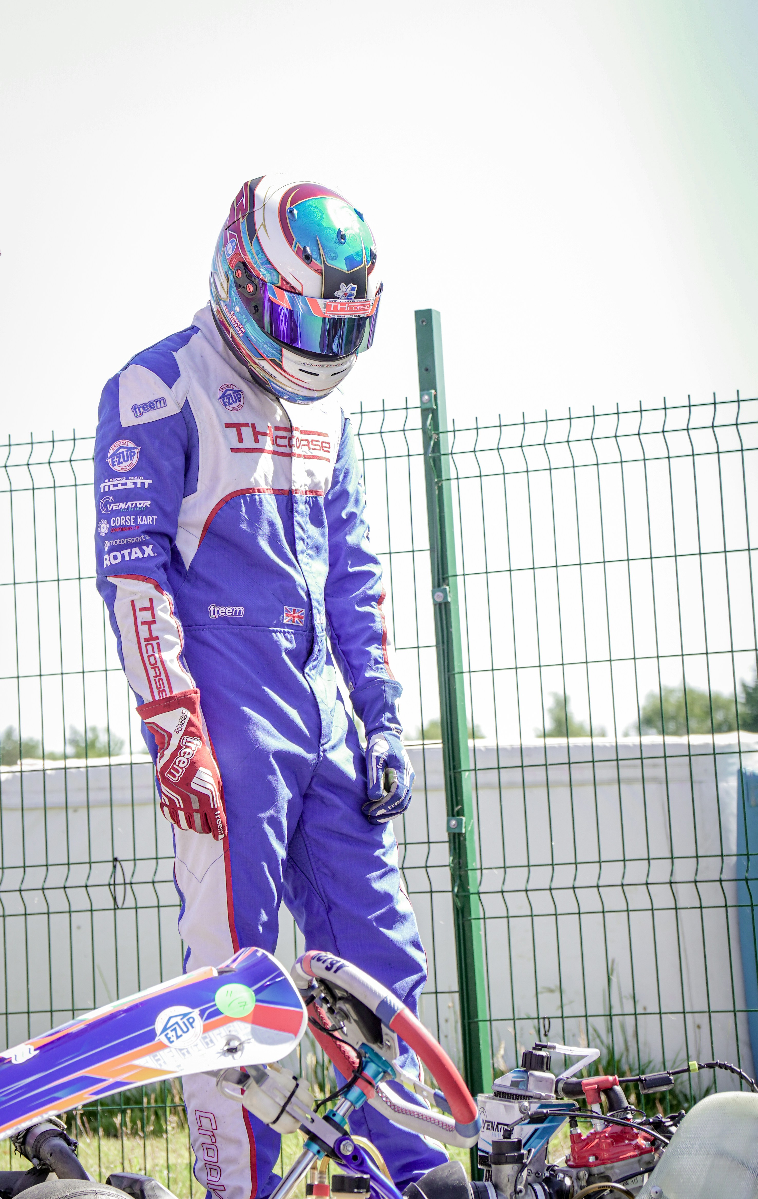Kart-Rennfahrer in voller Montur steht am Zaun.