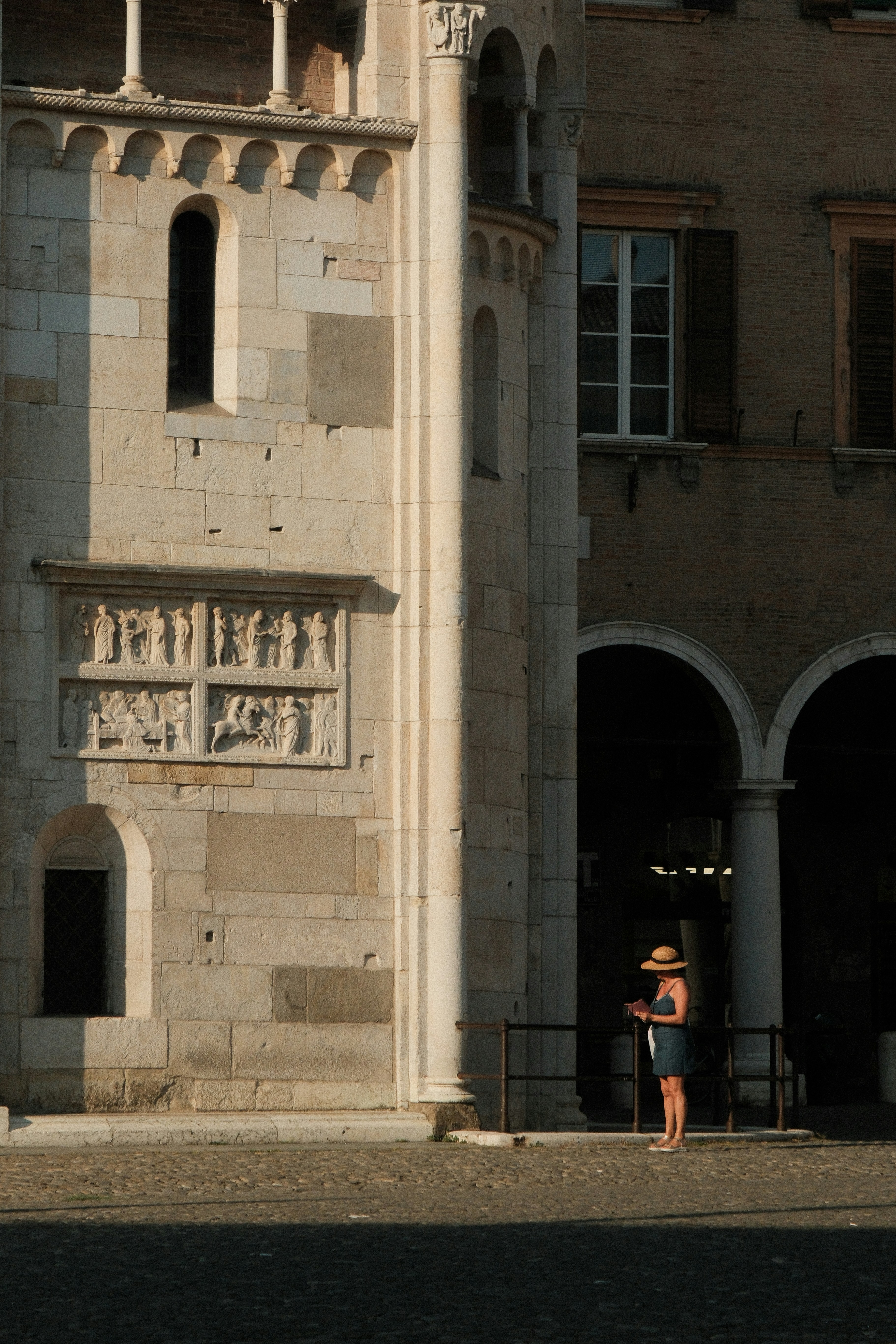 Woman stands under an archway next to a building.