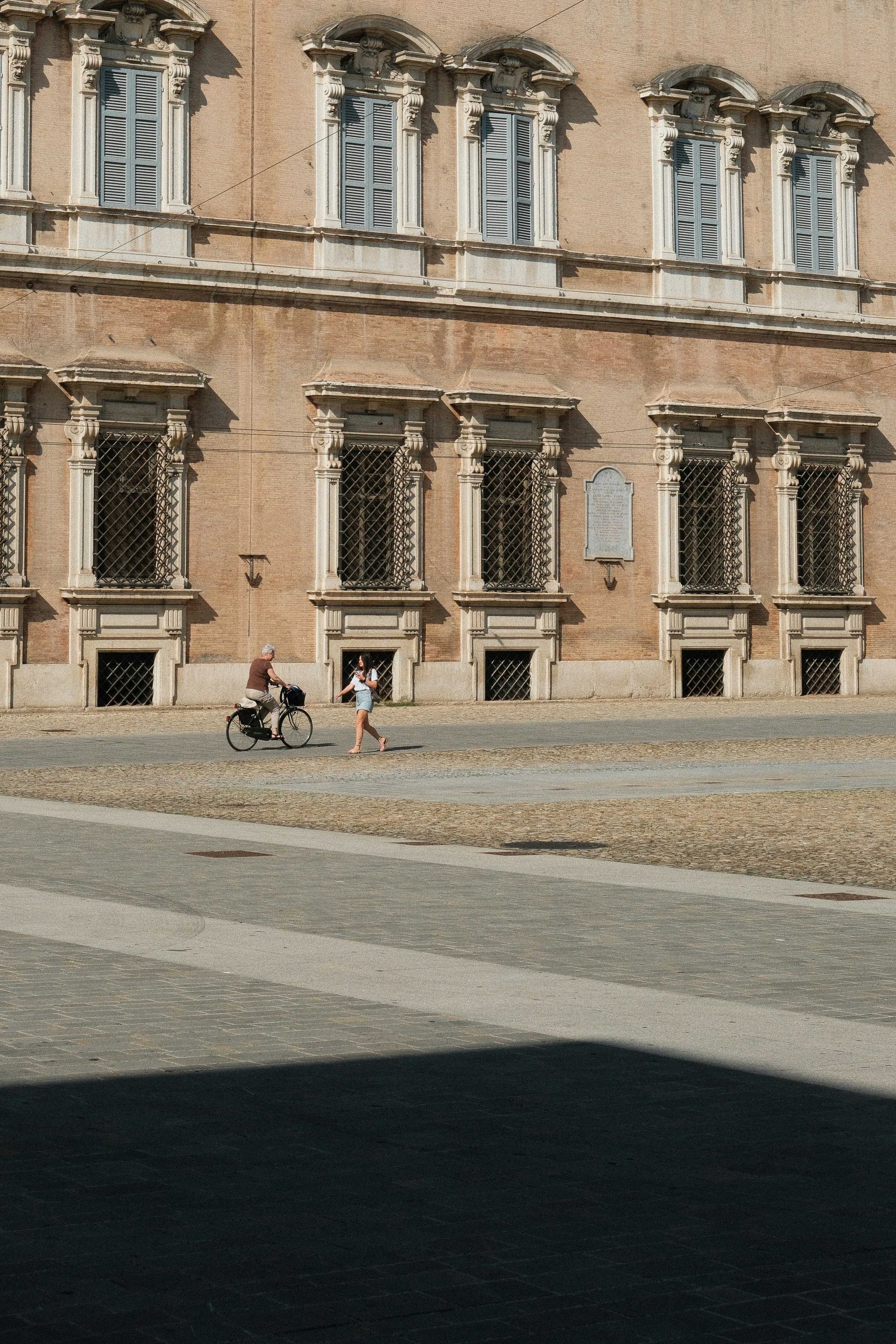 A person on a bike and runner by a building.