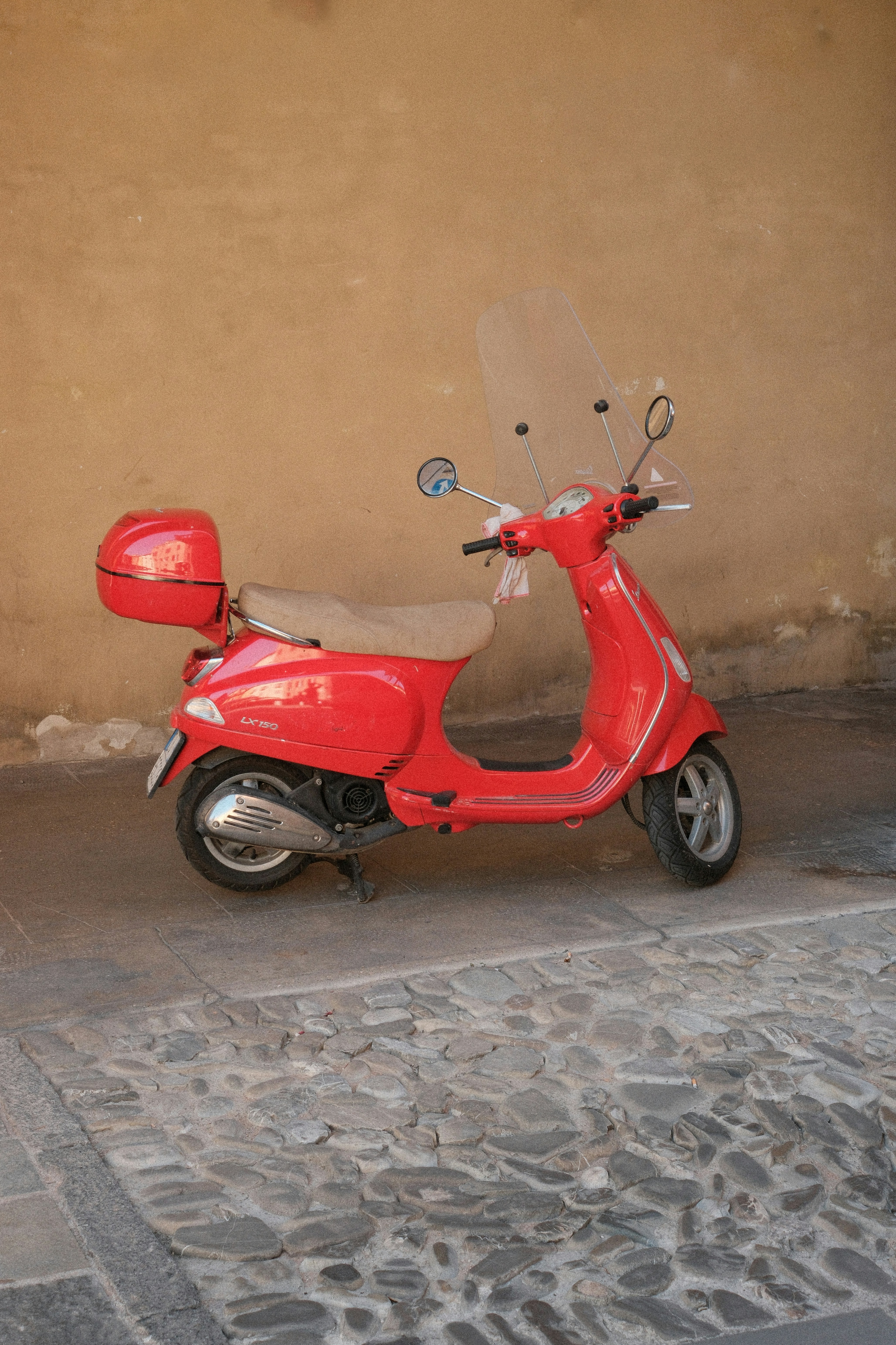 A red scooter is parked on a cobblestone street.