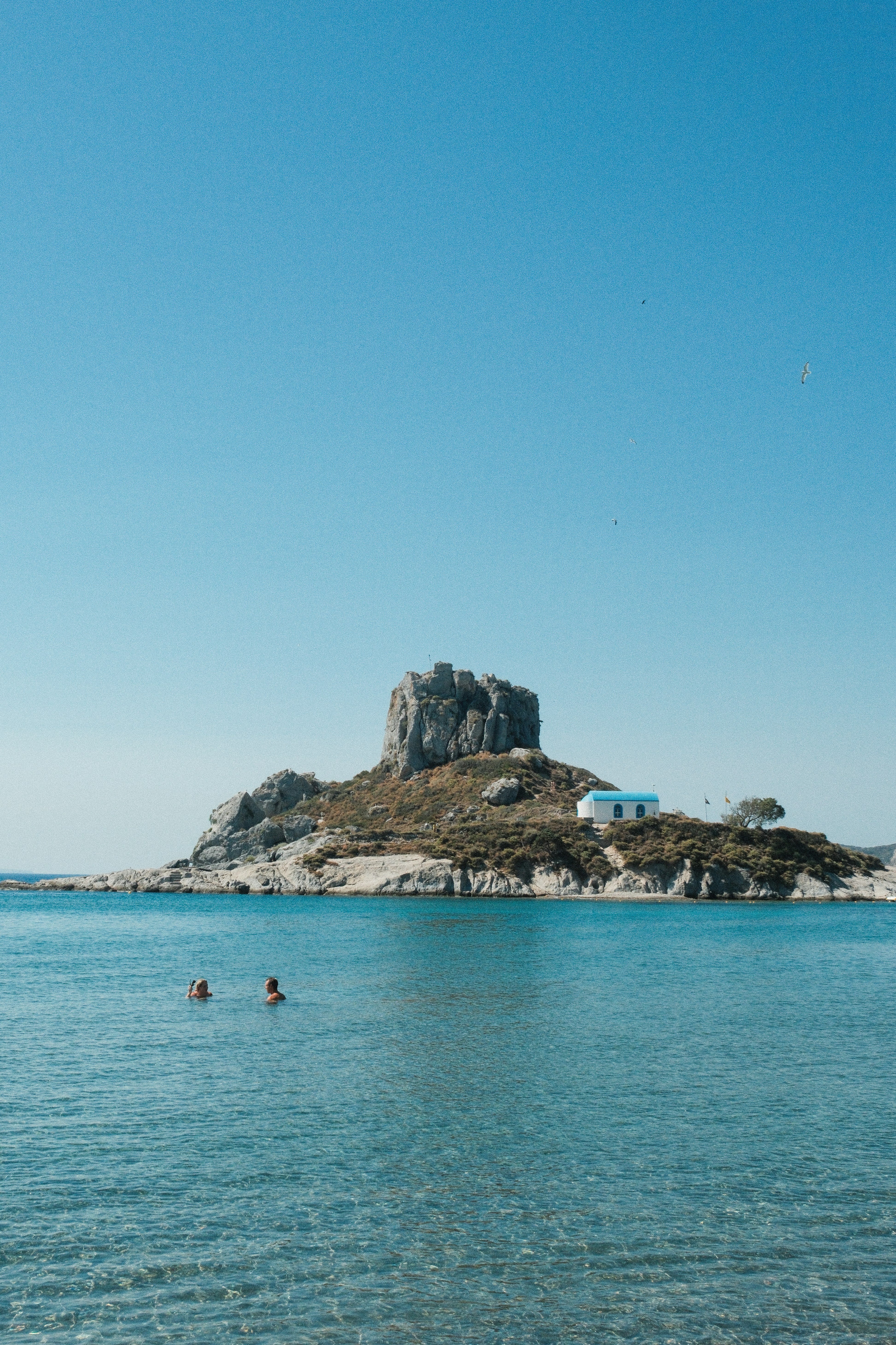 People swim near an island with a building.