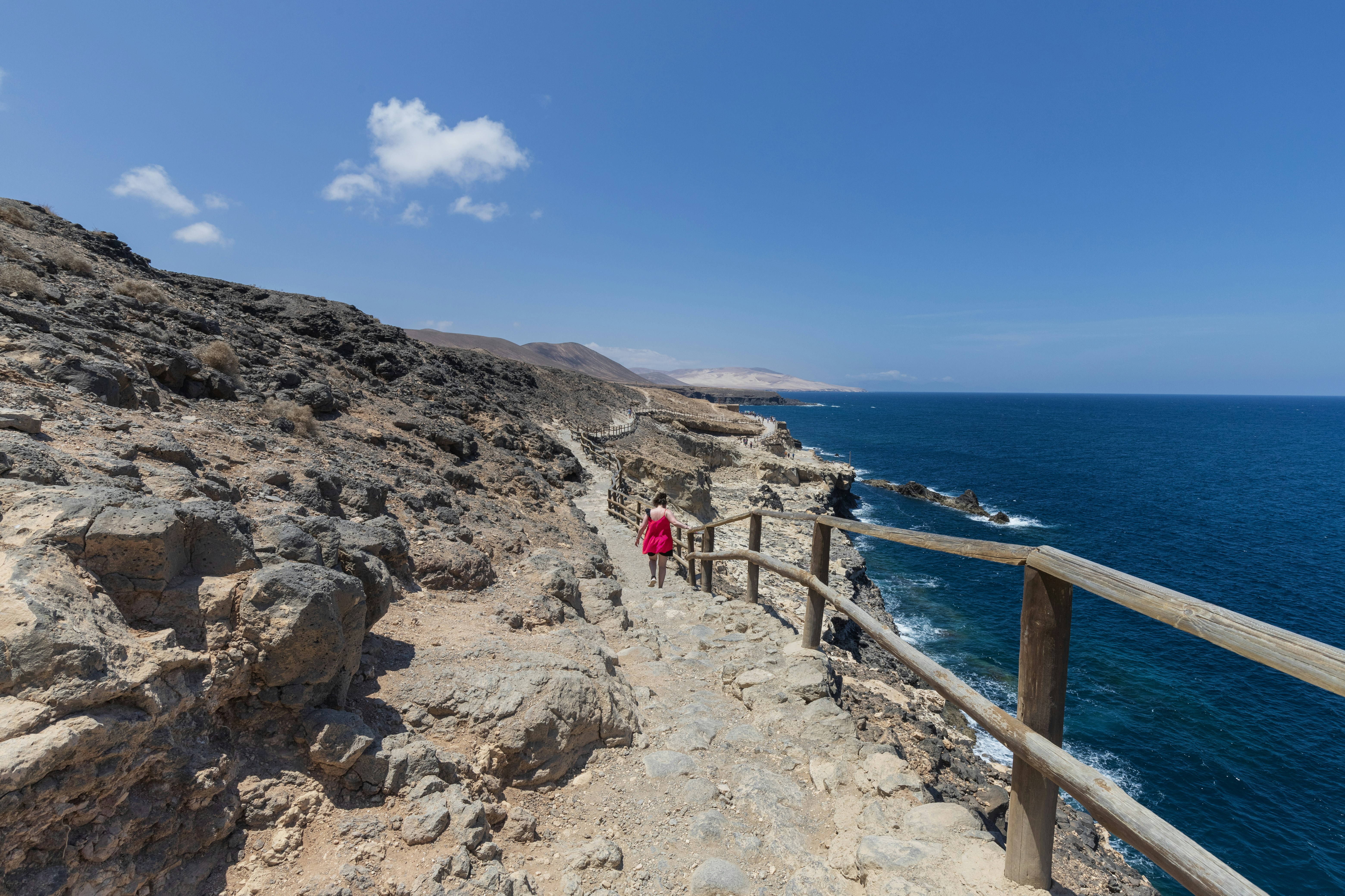 Woman walks along a cliffside path by the ocean.