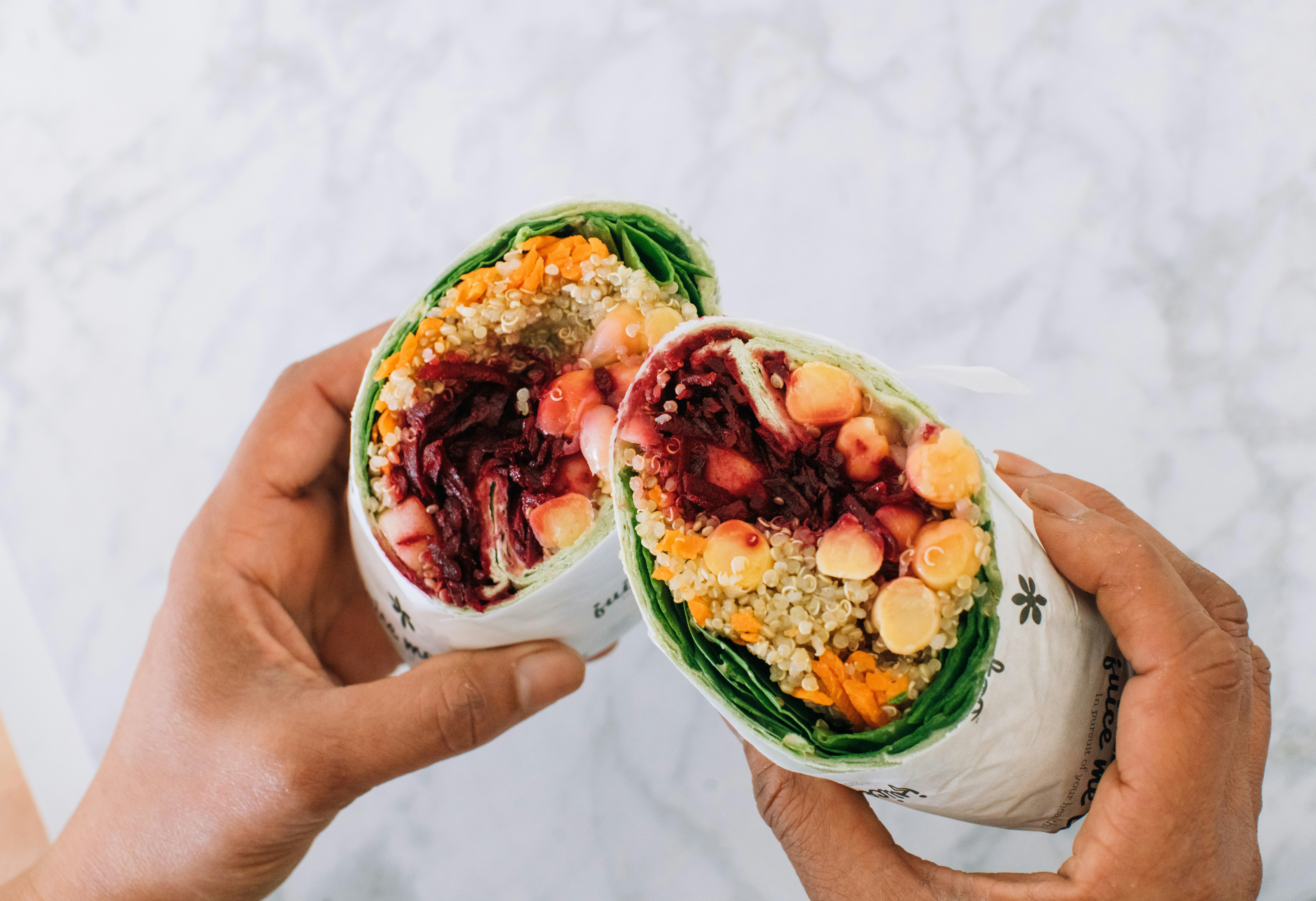 Hands hold a halved and loaded veggie wrap.