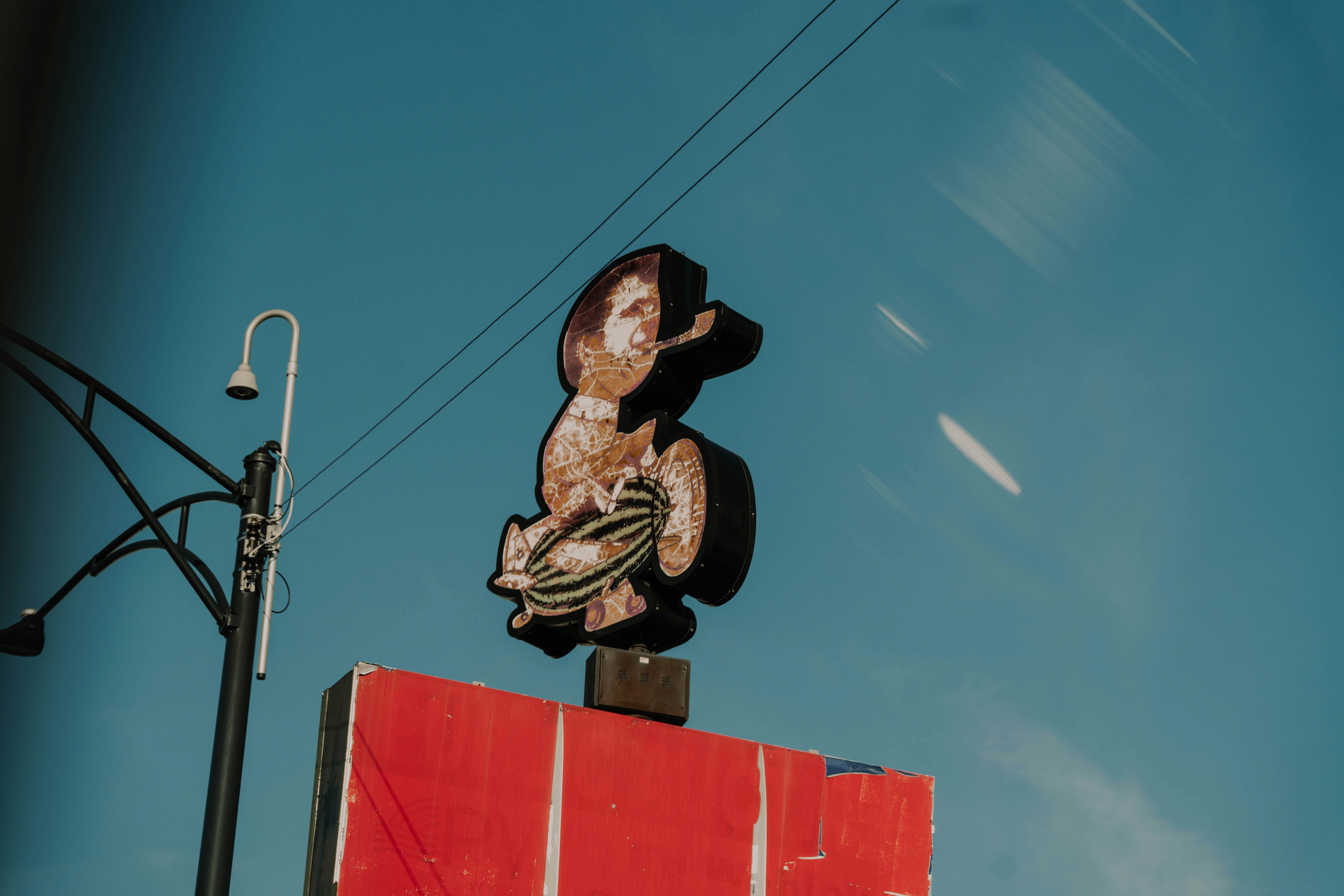 Weathered neon sign against a blue sky.