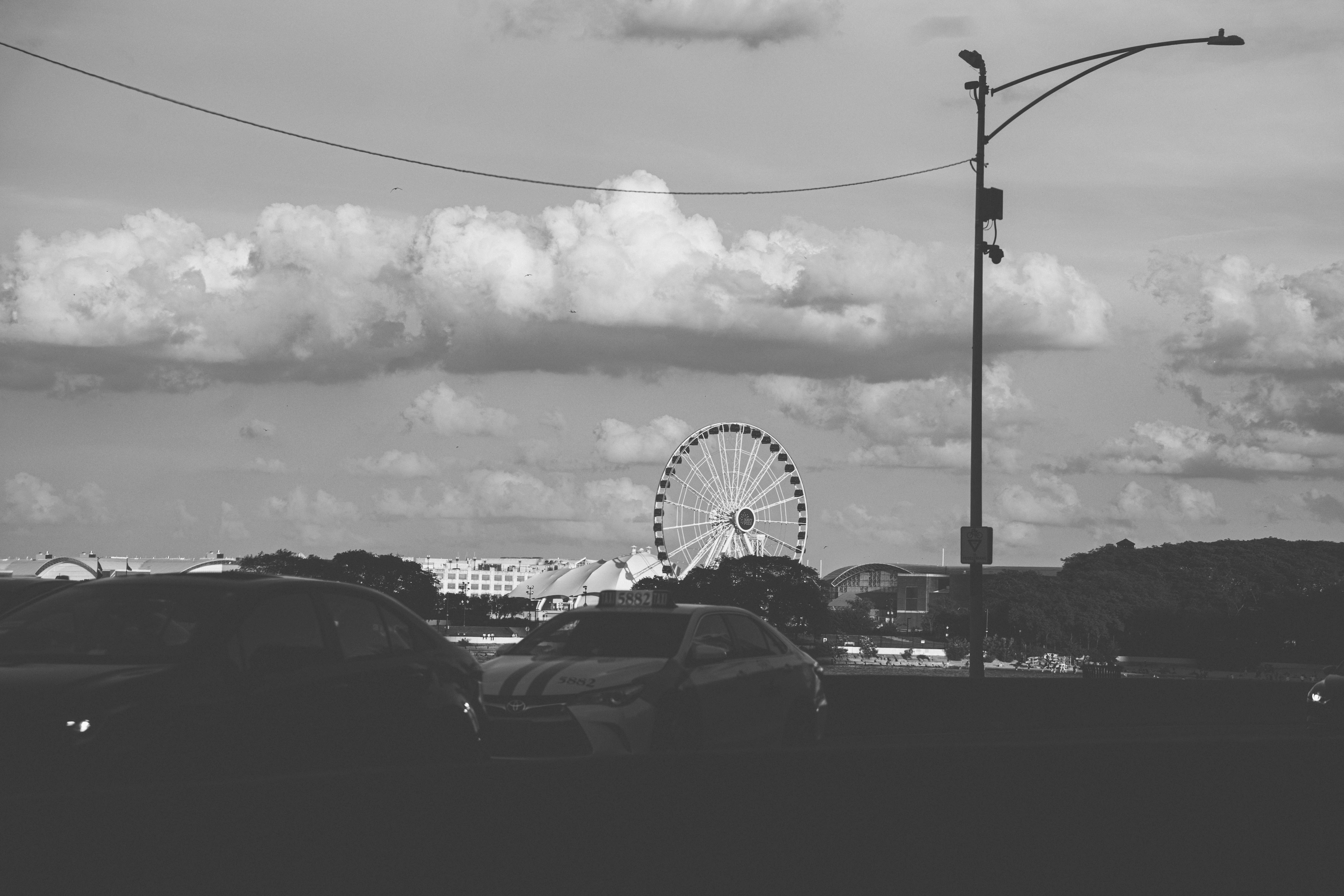 Ferris wheel silhouetted with cars under a cloudy sky.