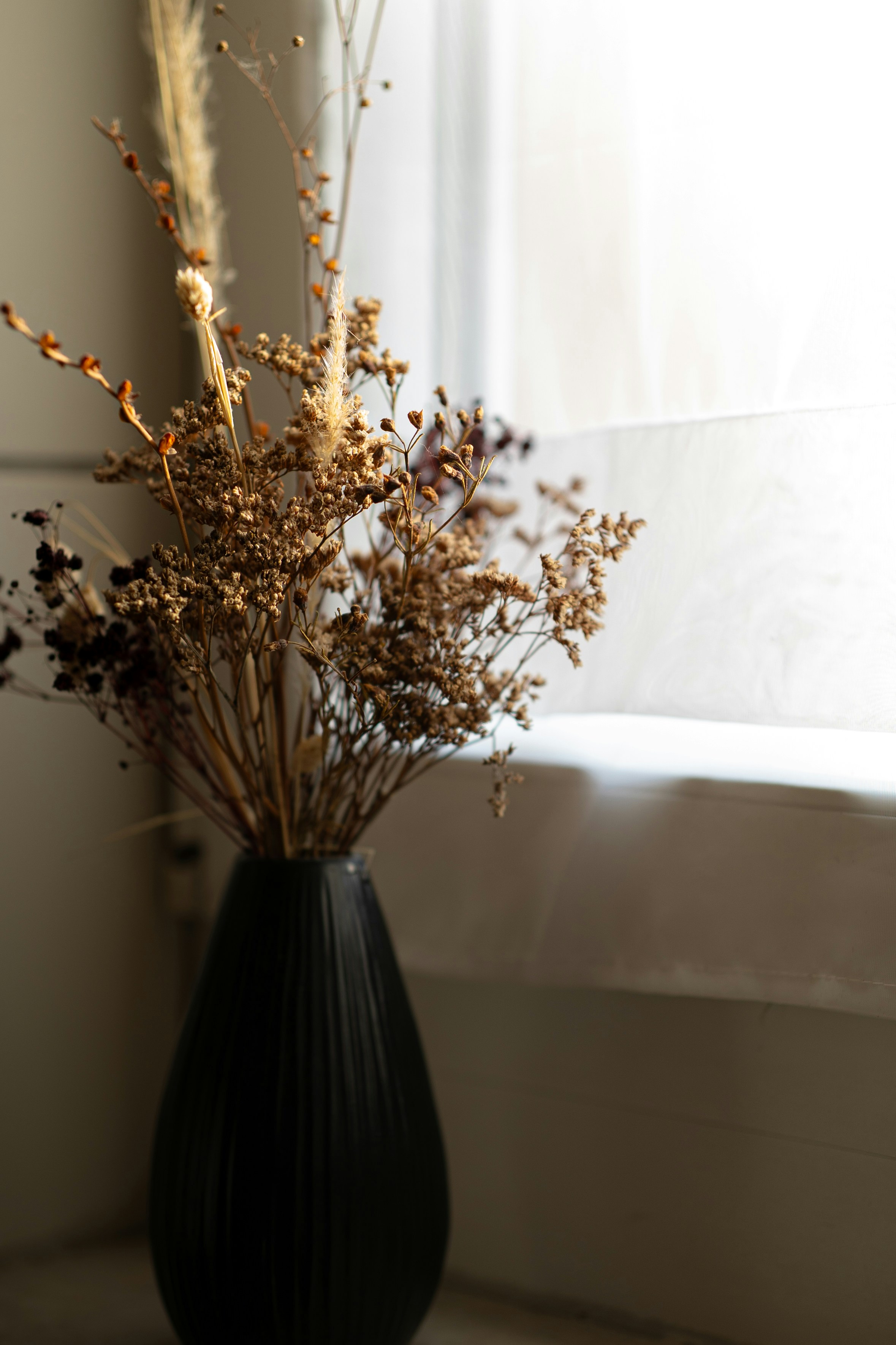 Dried flowers in a black vase by a window.