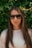 Young woman in sunglasses poses in front of leaves.
