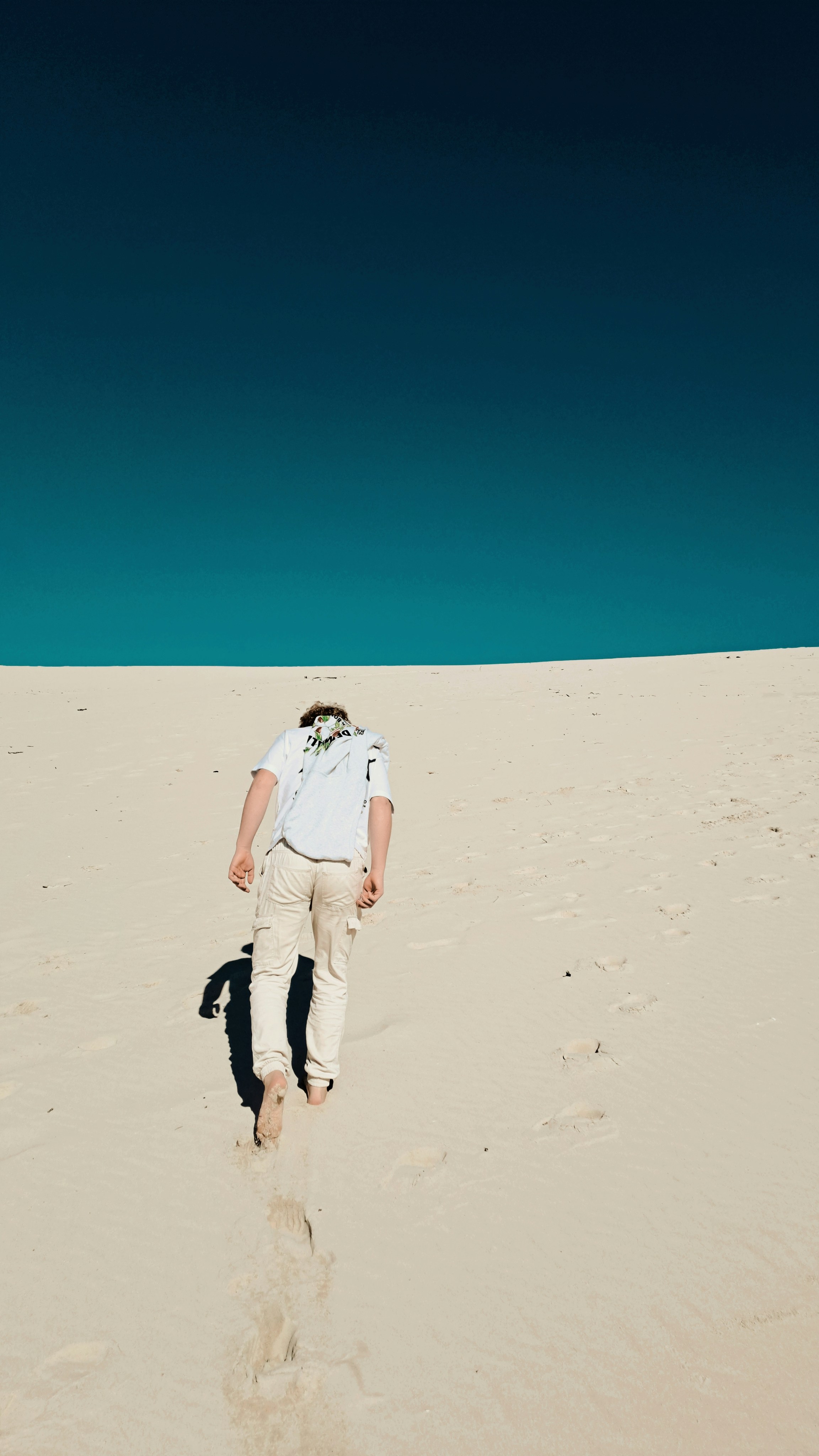 Um homem sobe uma duna de areia sob um céu azul brilhante.