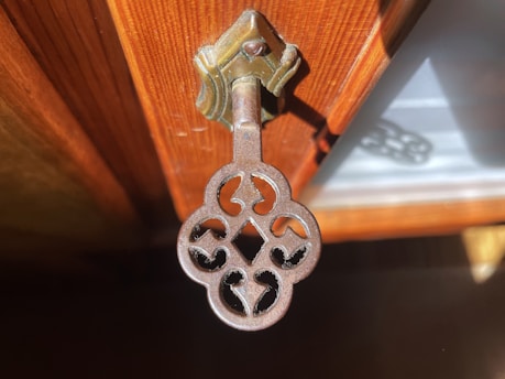An ornate key hangs from a wooden surface.