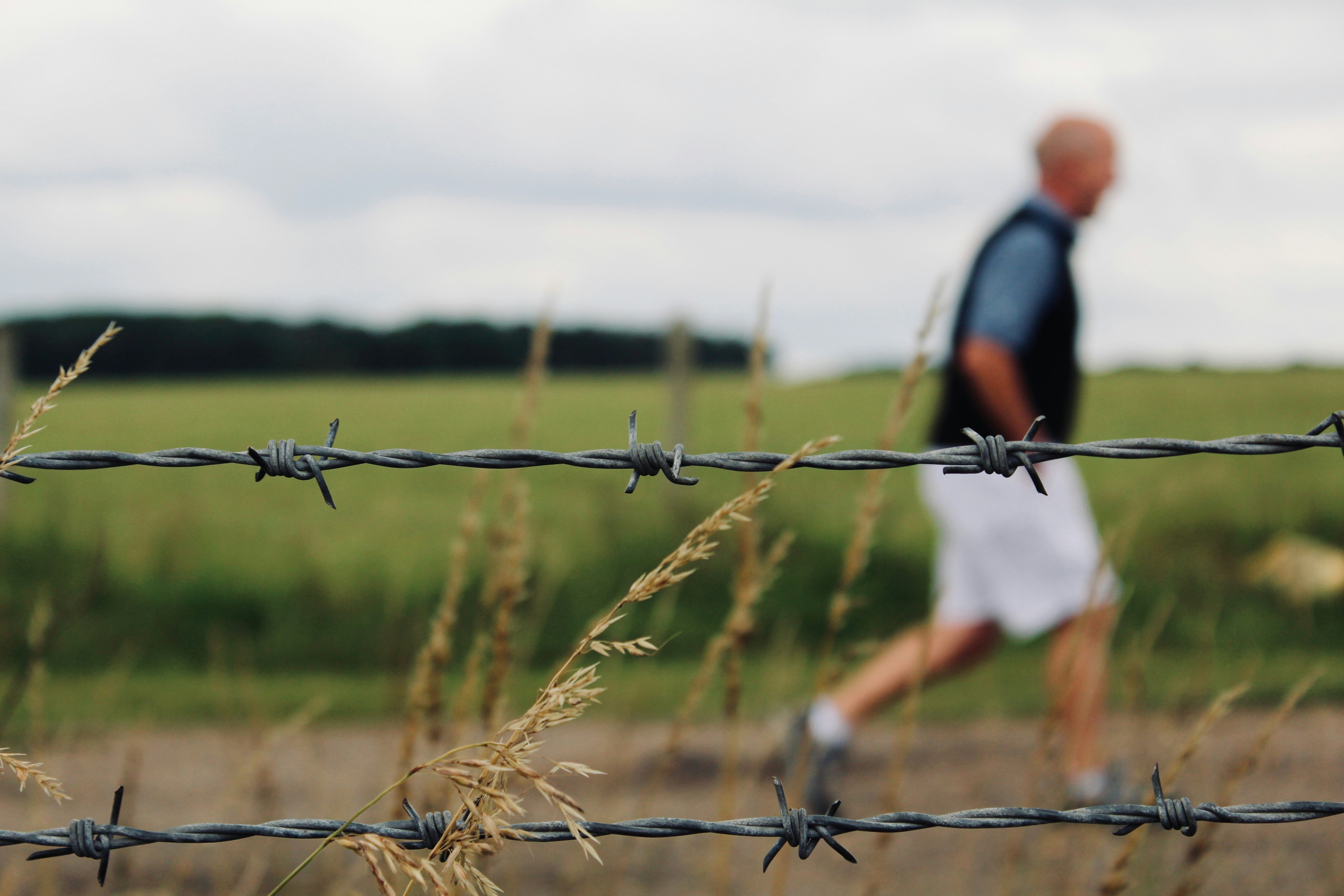 Barbed wire is in focus with a blurred man.