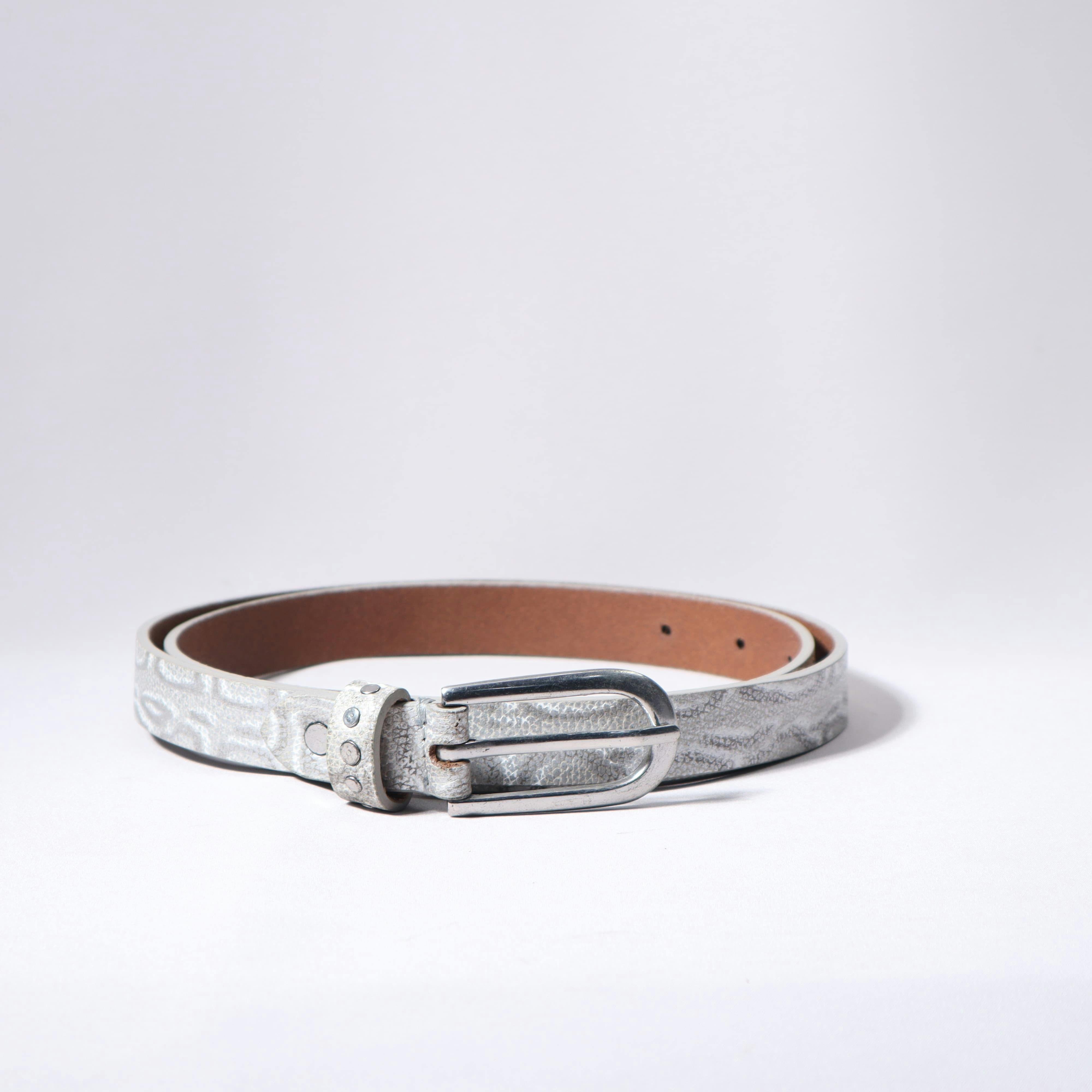 A stylish, silver belt lies on a white surface.