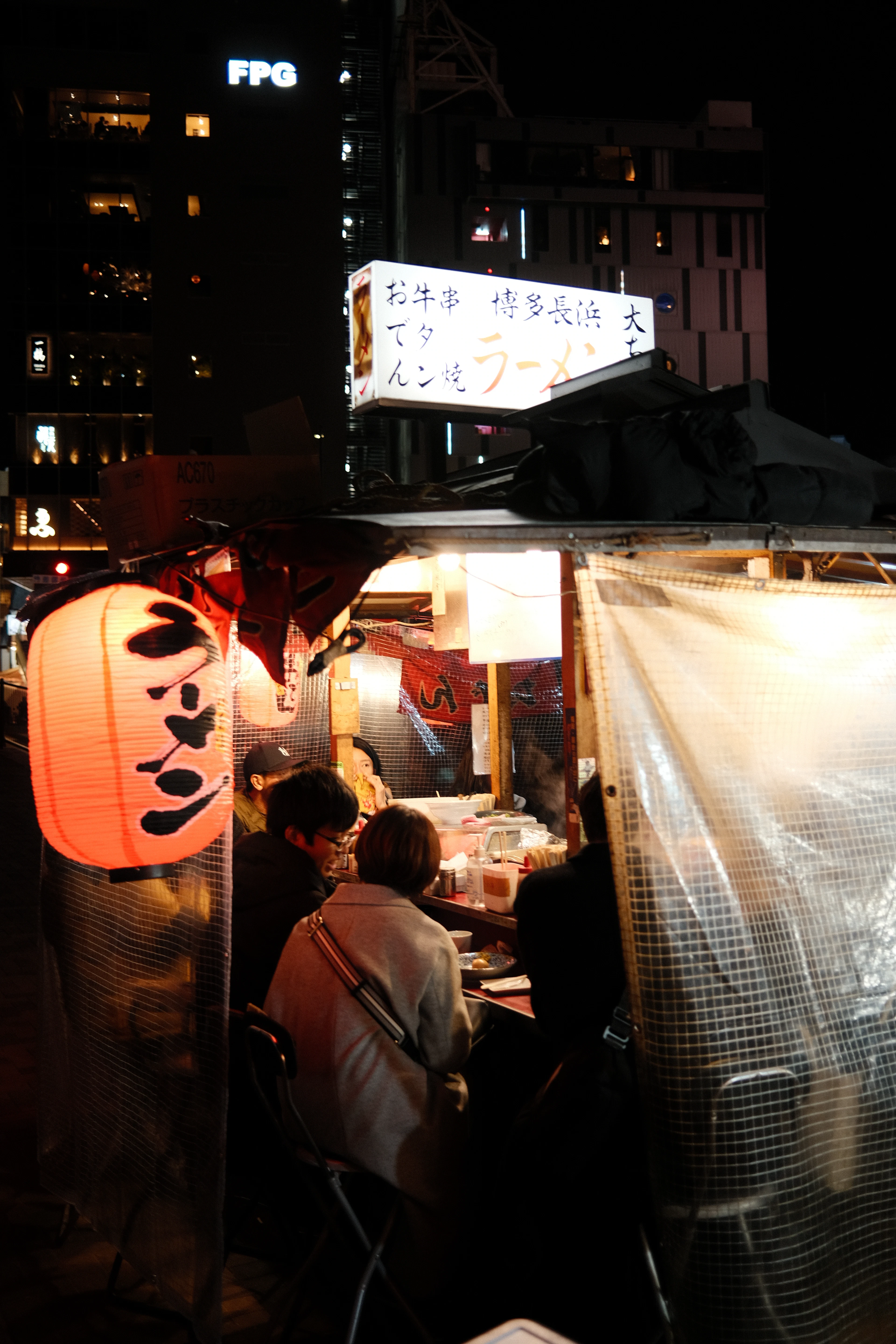 A glowing red lantern marked with ramen characters lights a Fukuoka yatai food stall at night.