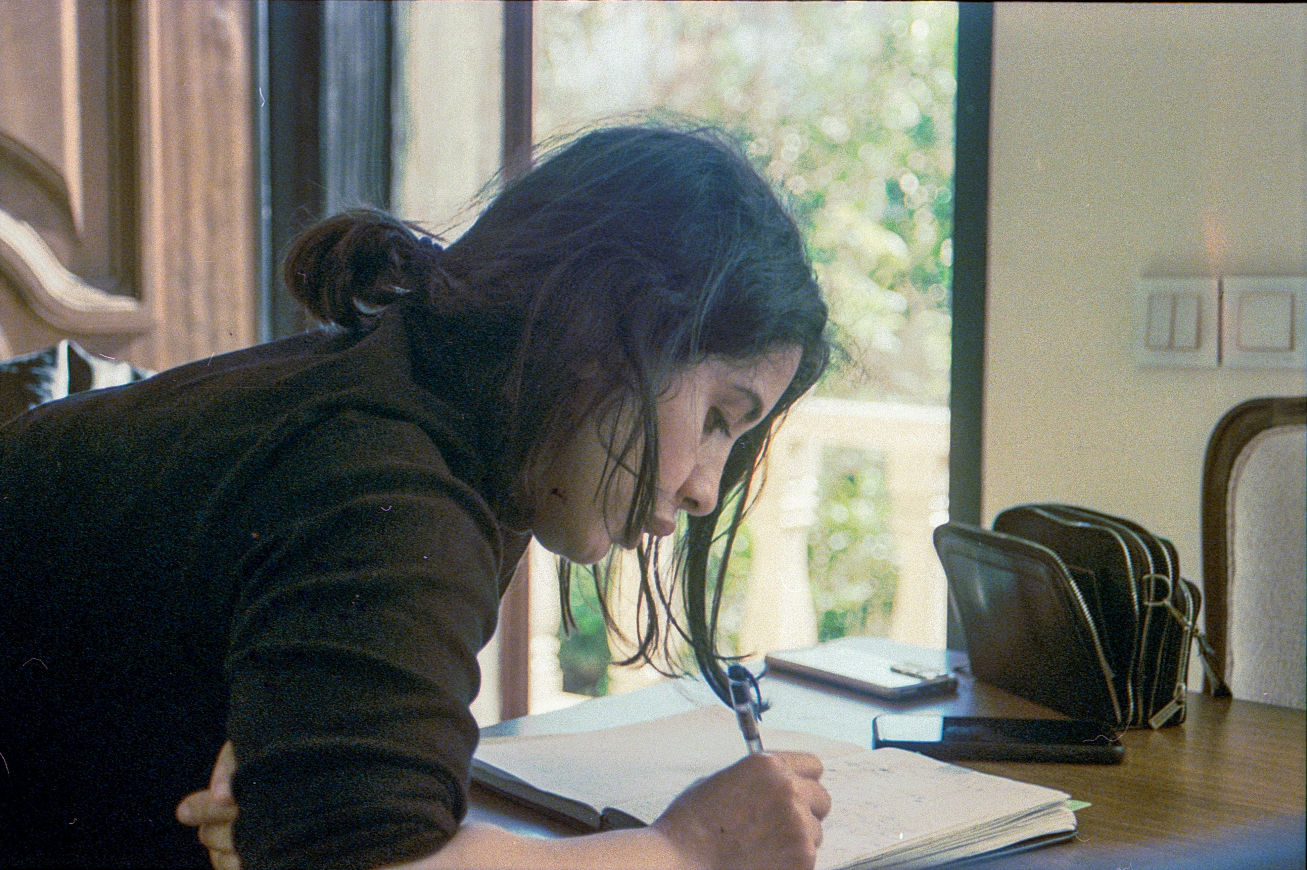 A person sitting at a desk, thoughtfully writing in a journal or notebook, with a pen in hand, suggesting introspection and self-reflection - cognitive behavioral therapy