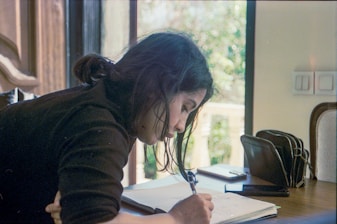 A woman writes in a notebook at a table.