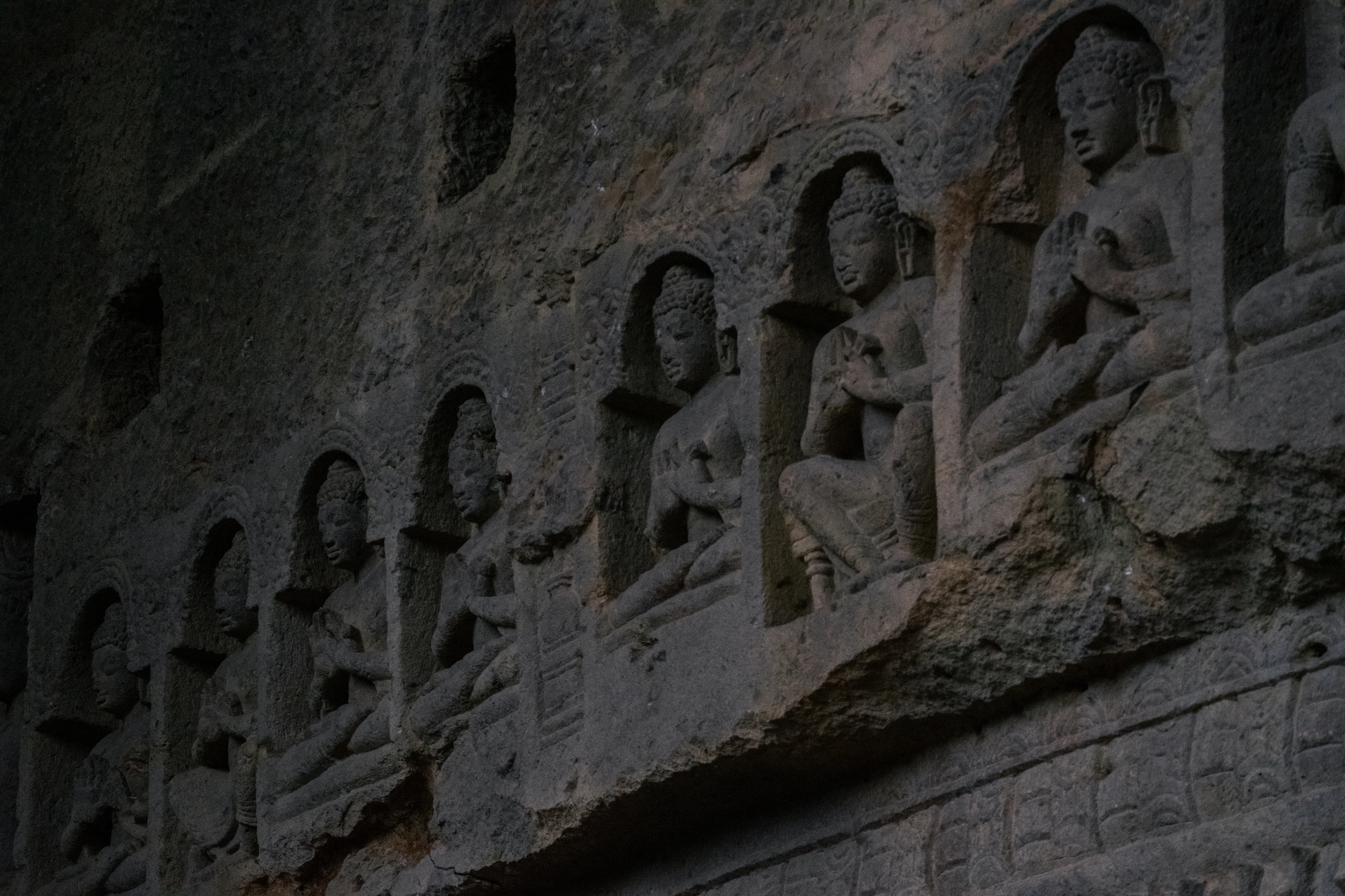 Rows of ancient rock-cut Buddhist relief carvings line a dark cave wall.