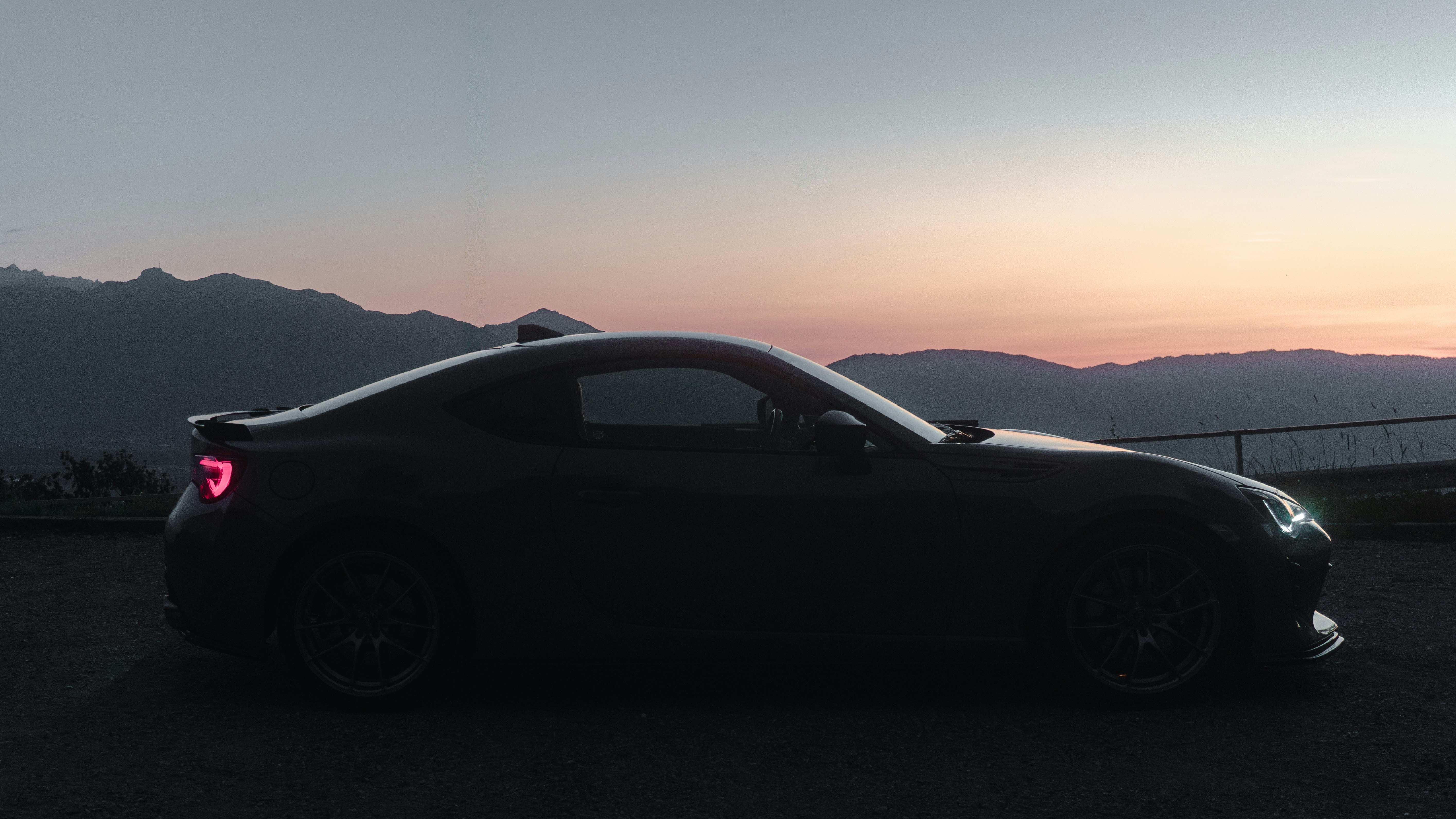 A dark sports car silhouetted at sunset.