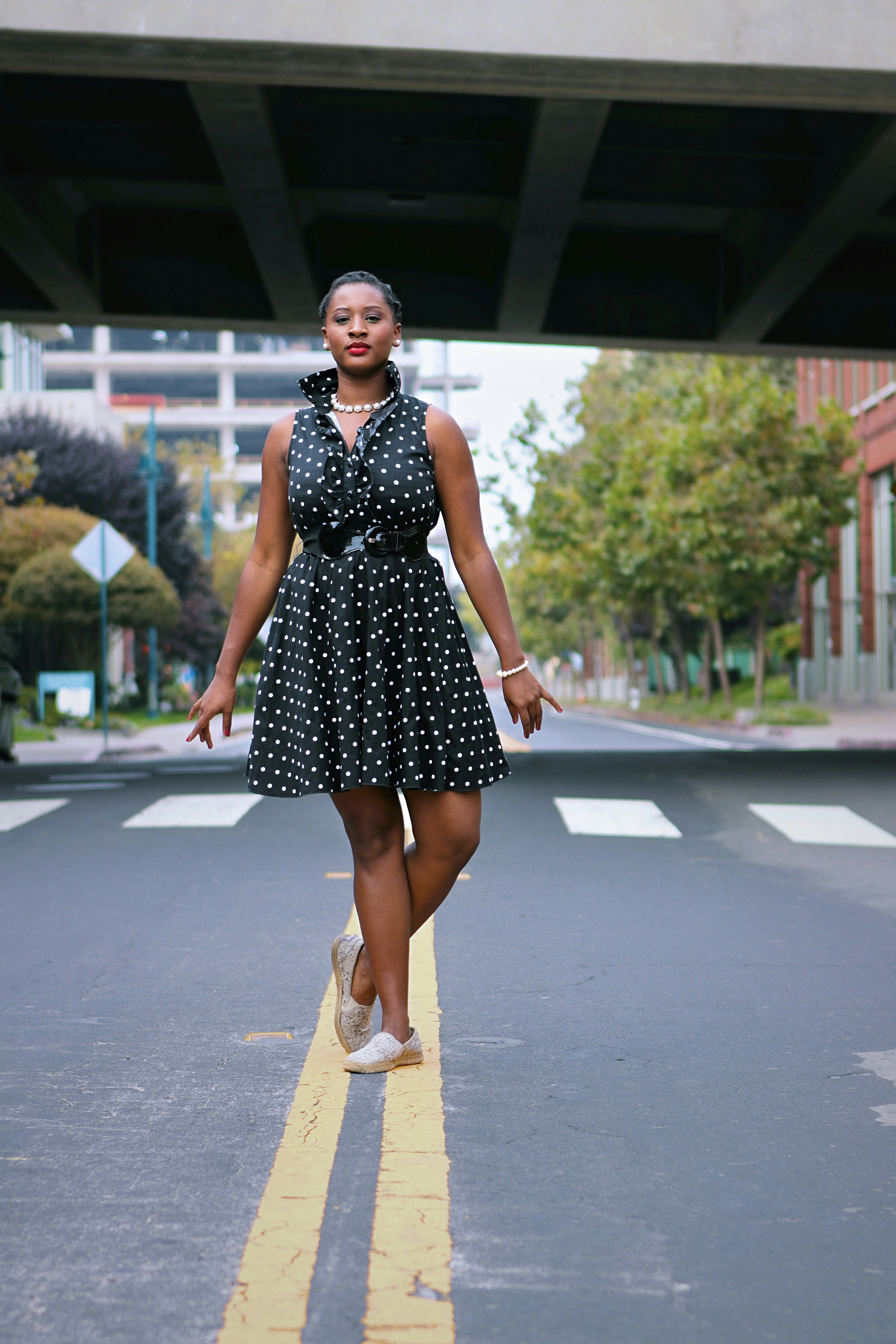 A woman in a dress poses on a street.