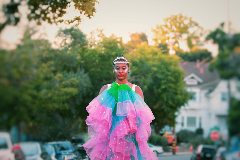 Femboy poses elegantly in a colorful dress outside