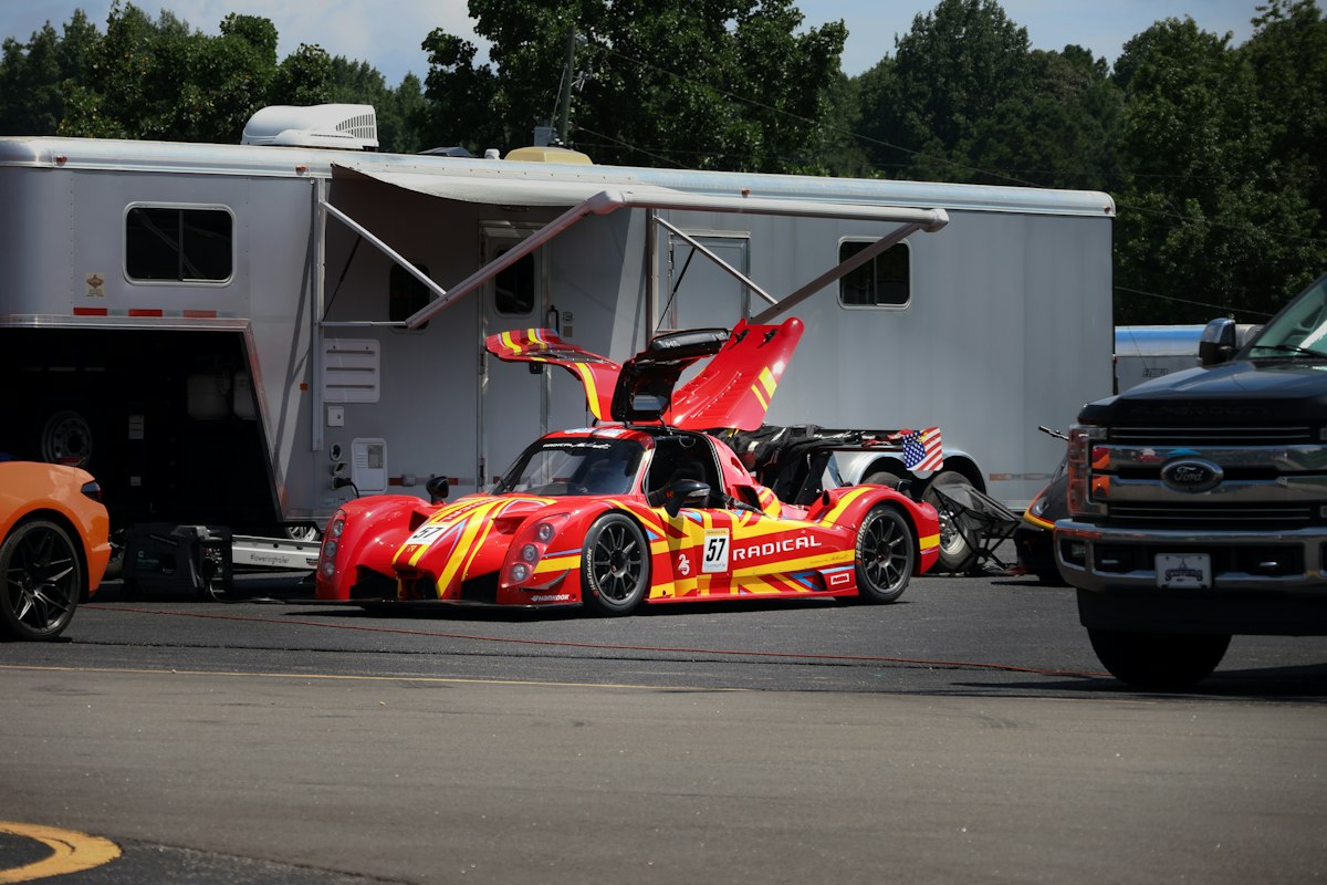 Prototype de course rouge et jaune portes ouvertes devant une remorque d'assistance dans un paddock