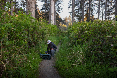 A person kneels on a forest path.