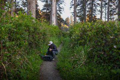 A person is kneeling on a forest path.