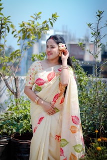 A woman poses in a saree, holding a flower.