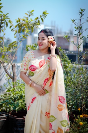 A woman poses in a saree, holding a flower.