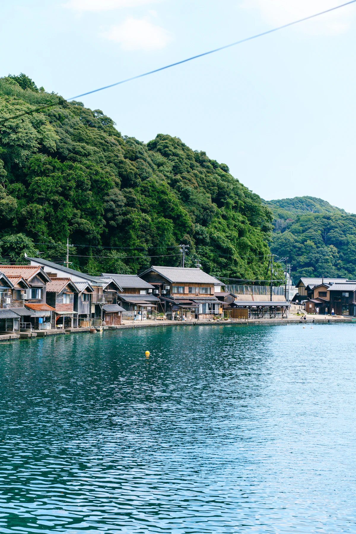 Funaya boathouses at the water's edge beneath green hills in Ine
