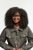 A smiling woman with curly hair wears glasses.