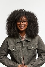 A smiling woman with curly hair wears glasses.