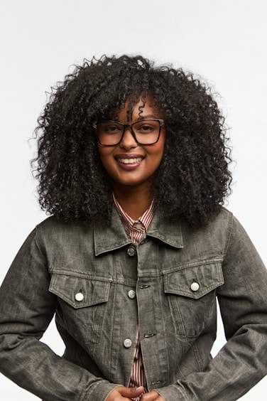 A smiling woman with curly hair wears glasses.