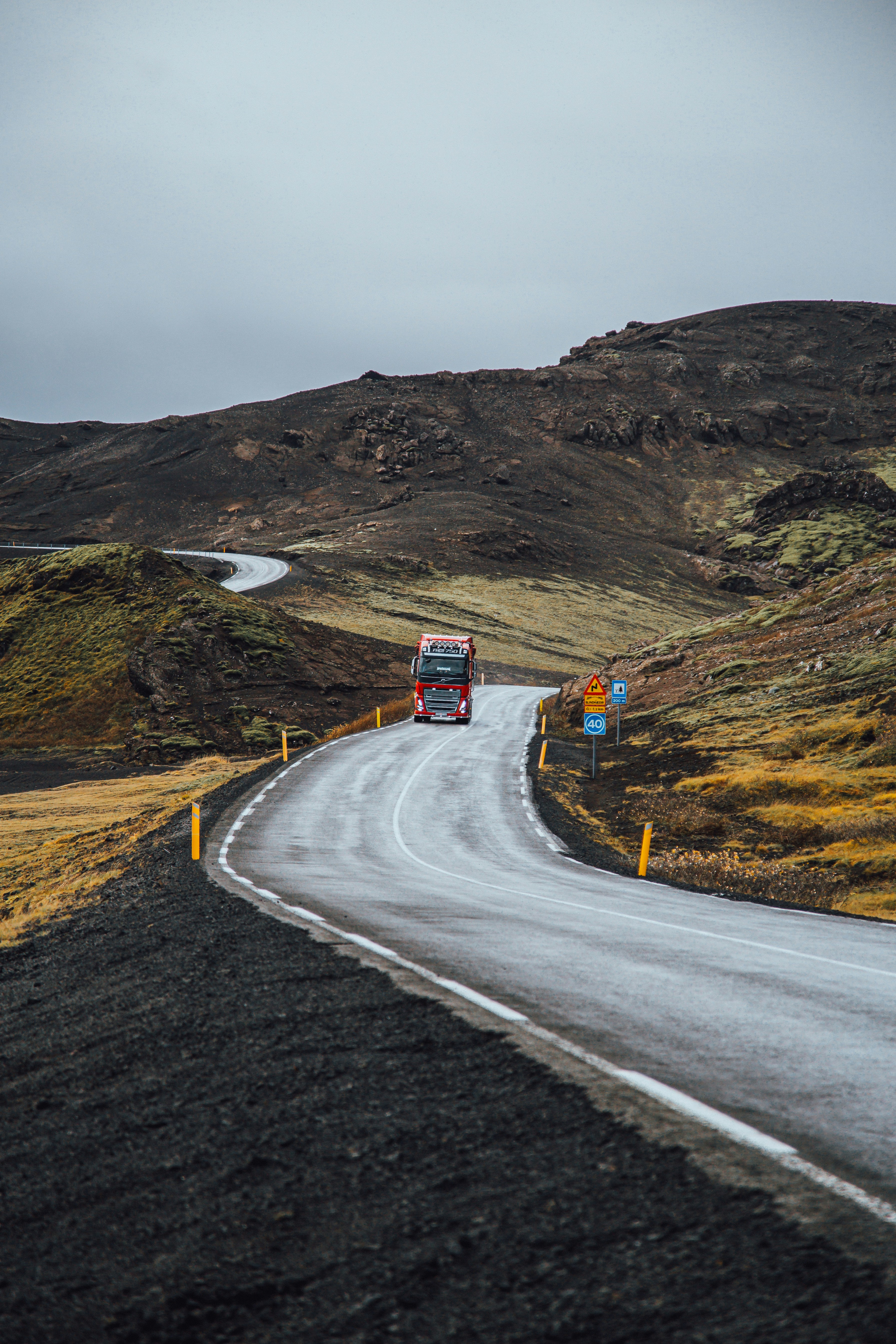 A truck drives on a road through rolling hills.