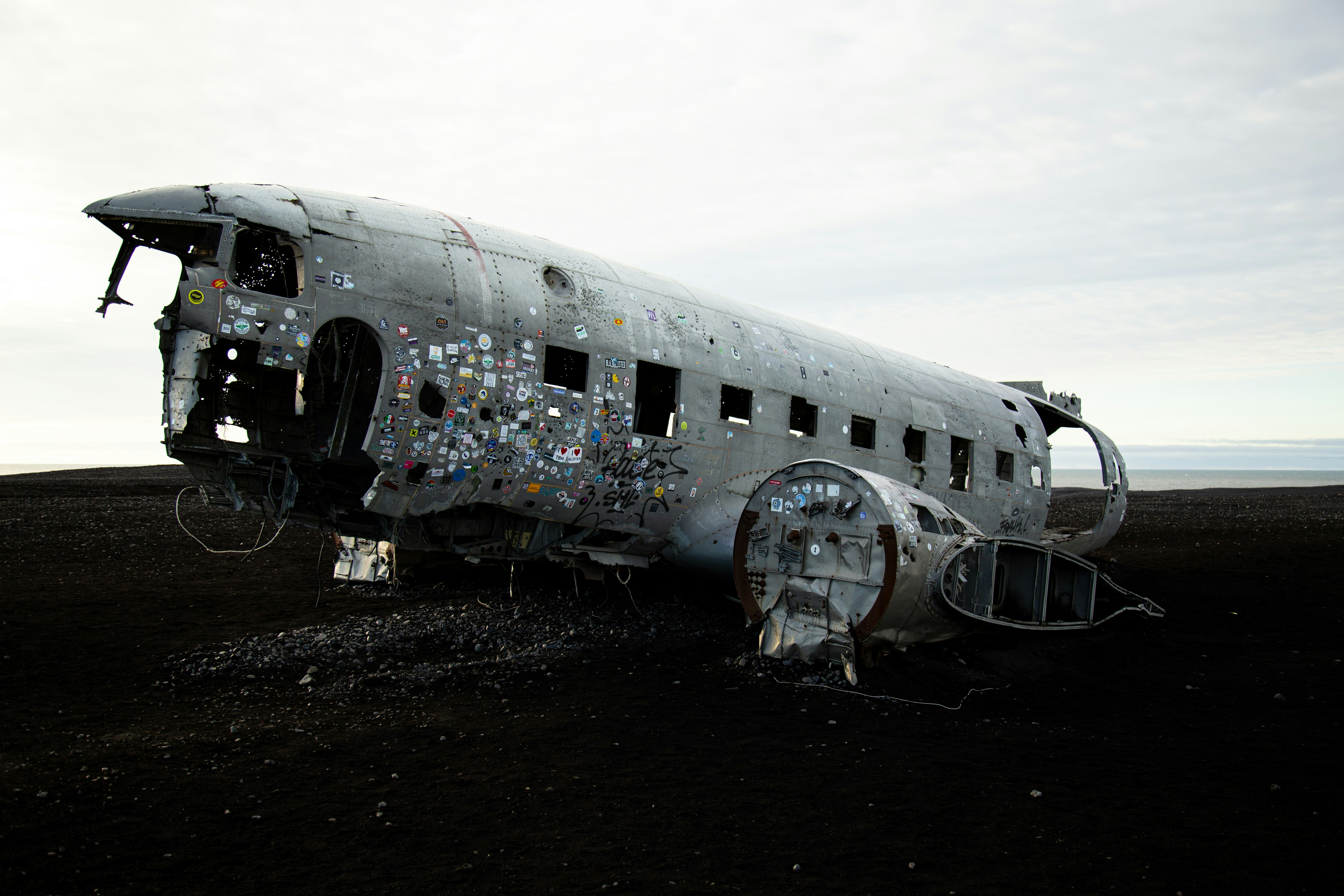 A plane wreck sits on a black sand beach.