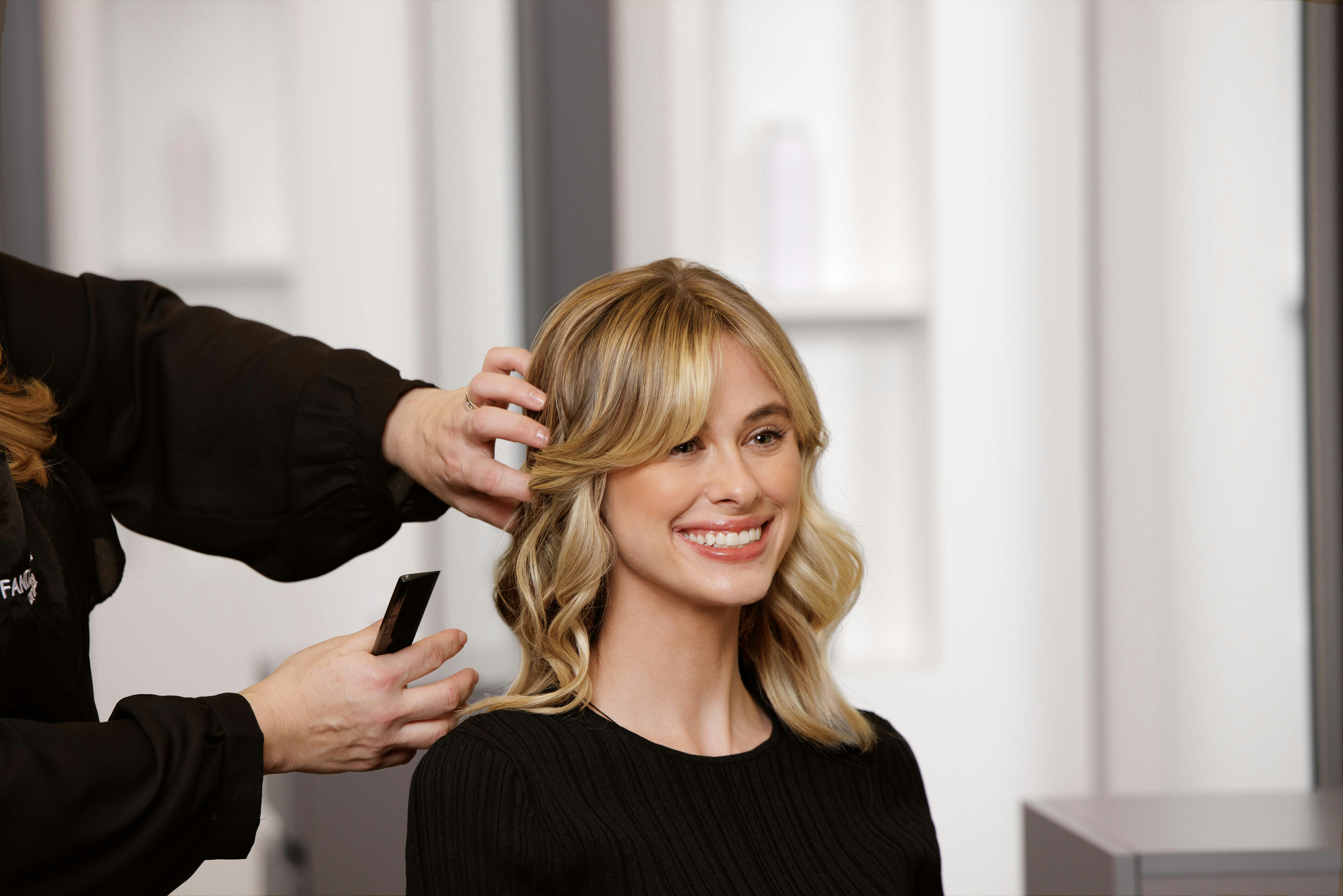 Hair stylist adjusting blonde waves with hand-sewn weft extensions