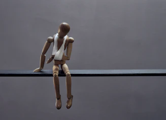 A wooden mannequin sits sadly with a bandage.