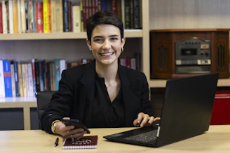 A woman smiles while working on a laptop.