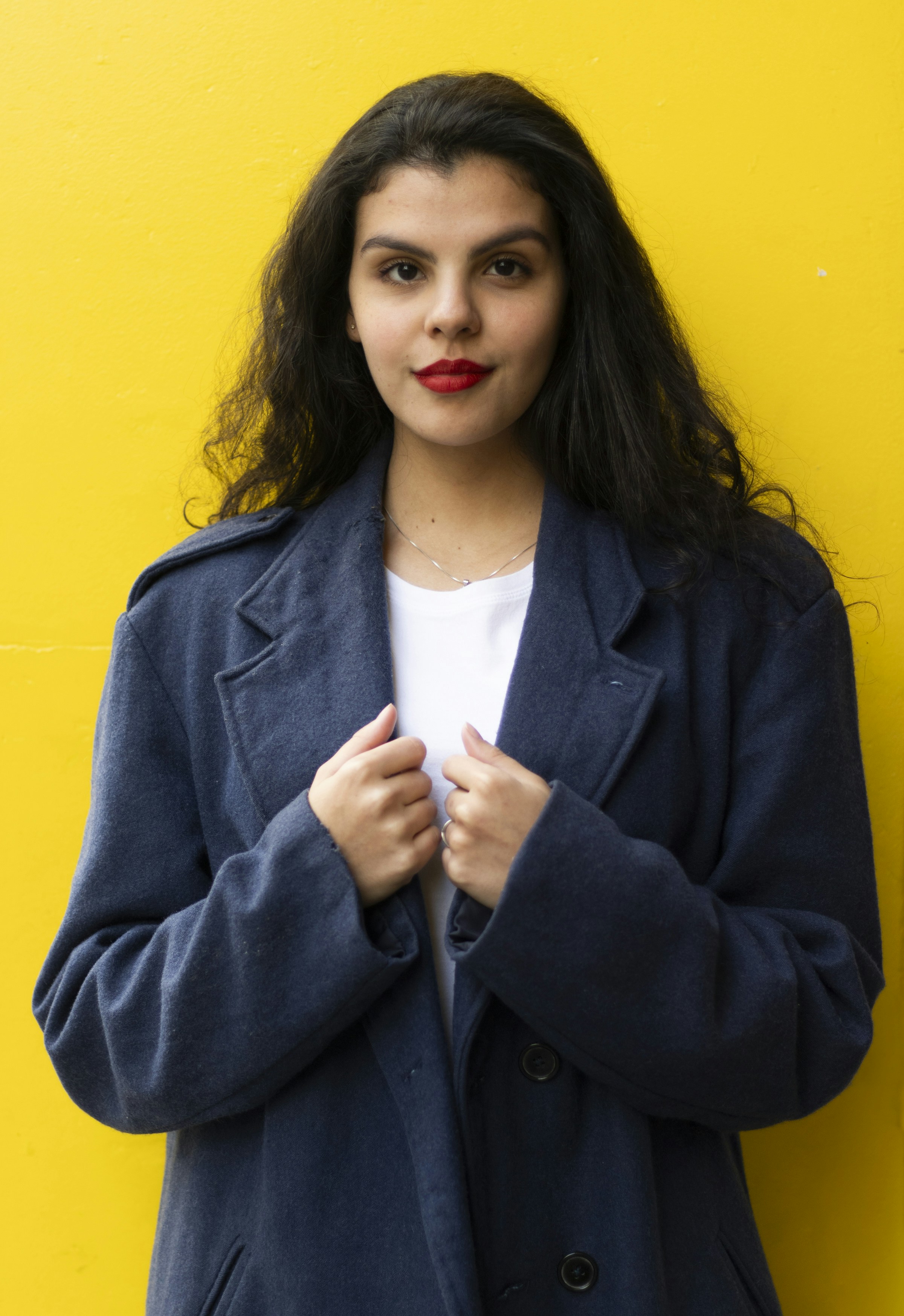 Woman poses in front of a bright yellow wall.