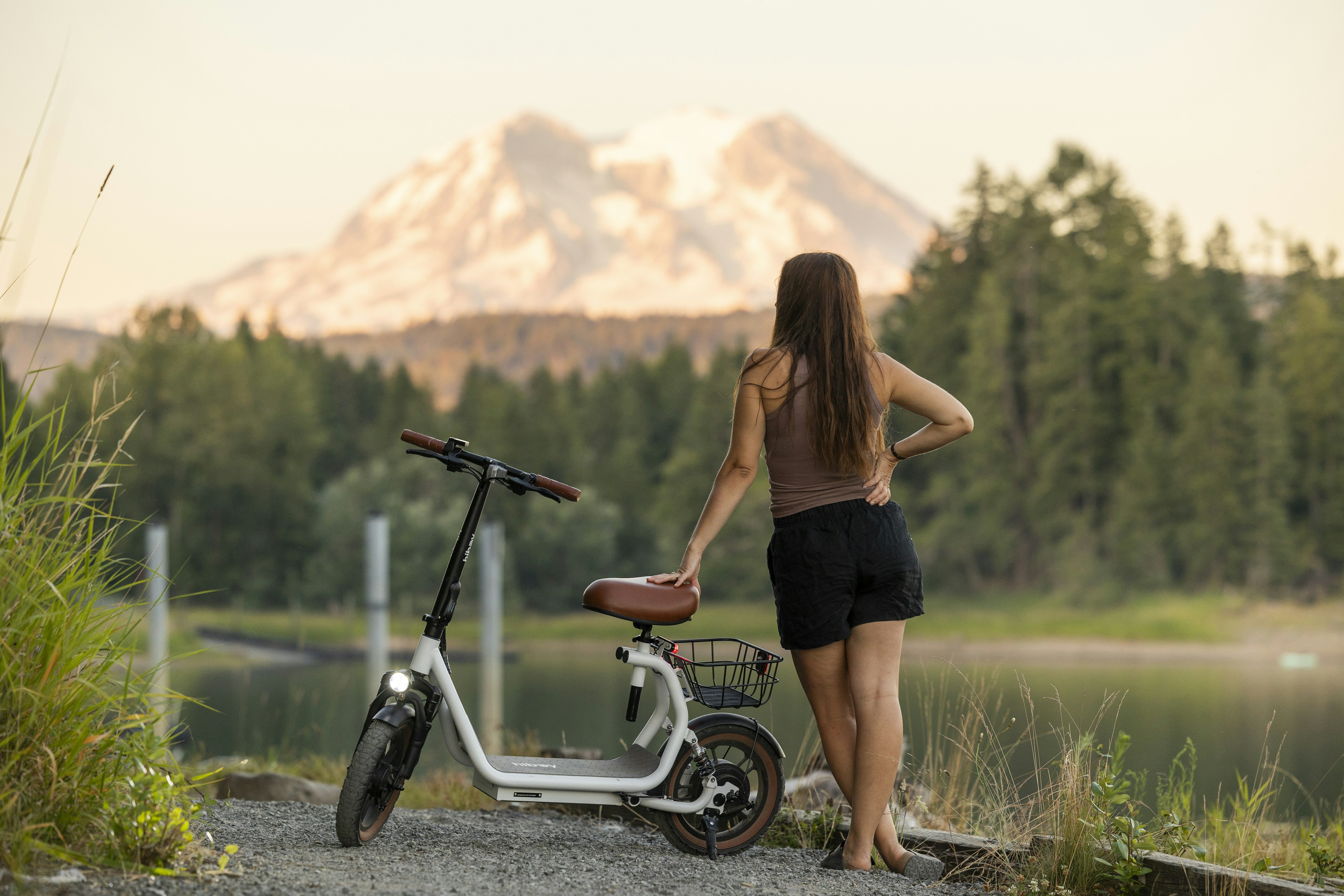 Woman enjoys view with scooter and mountain.