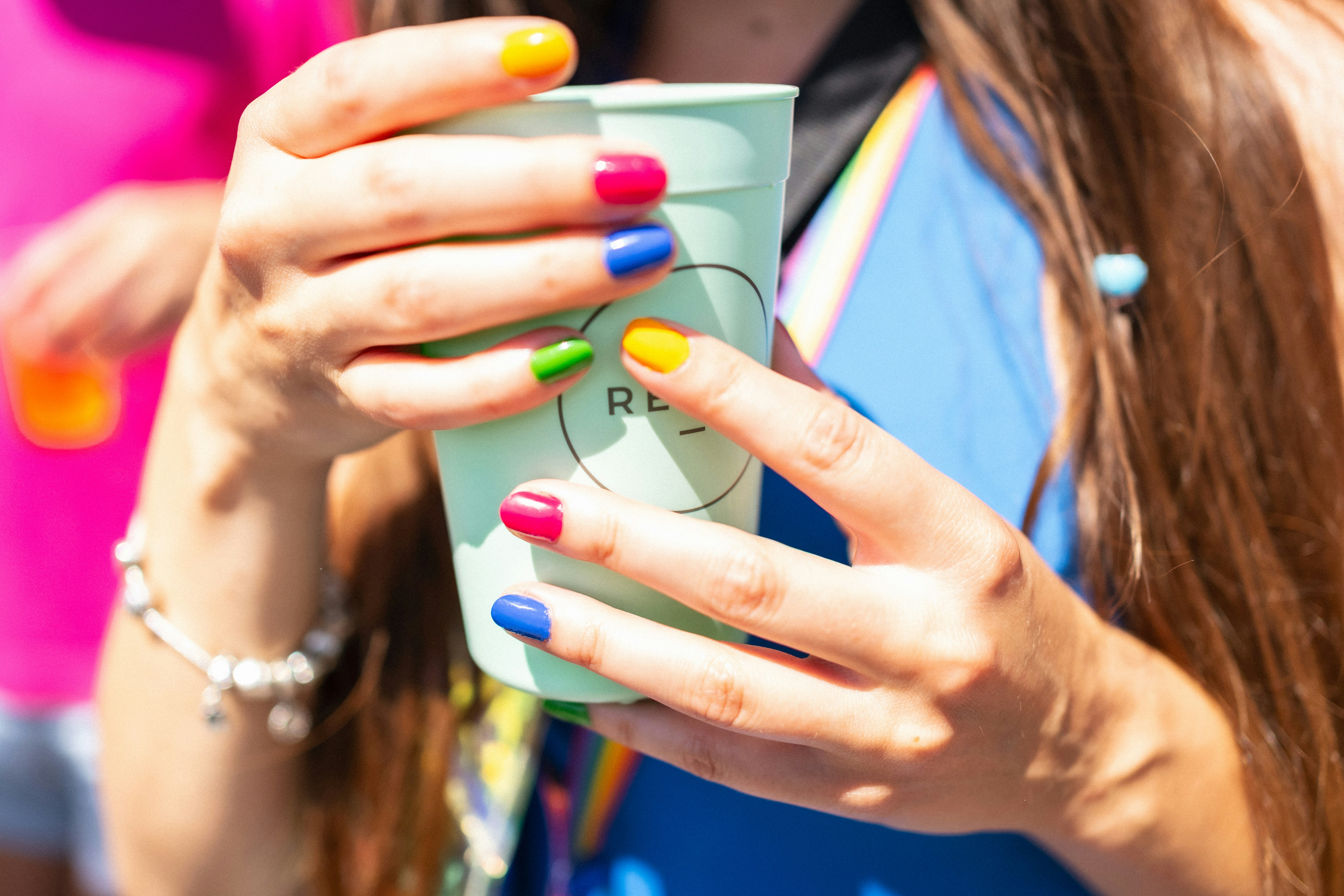 Woman's hands holding a cup with rainbow-colored nails