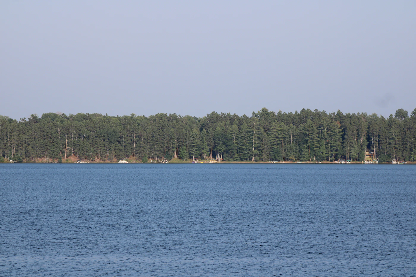 Calm Wisconsin lake reflecting a dense conifer shoreline under an open sky