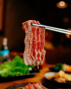 Fresh raw bacon held with tongs.