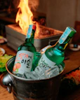 Korean soju bottles chilled in ice with grill background.