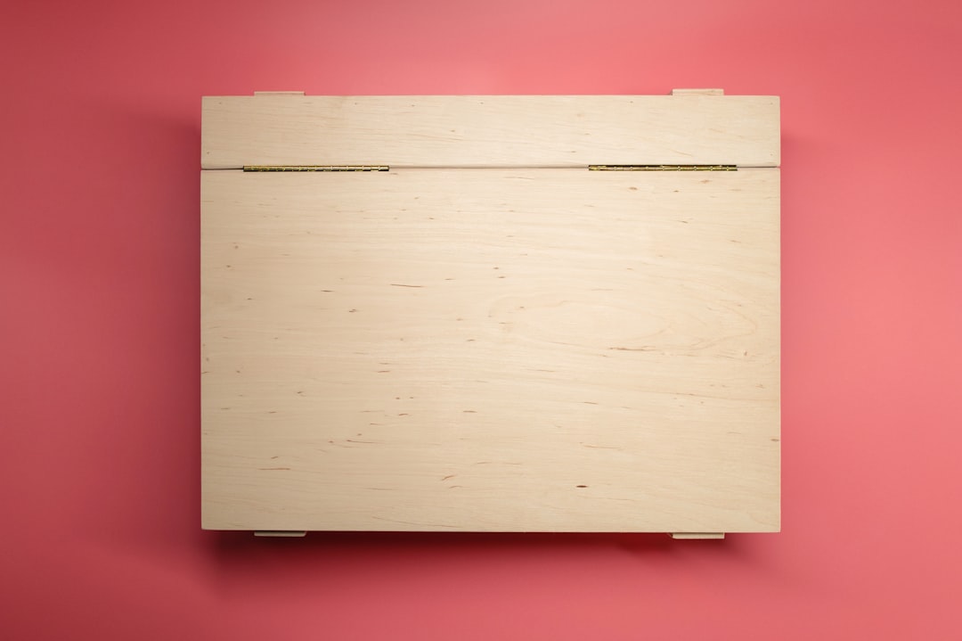 A closed wooden box sits against a pink background.