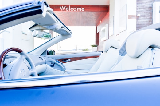 Convertible car parked under a "welcome" sign.