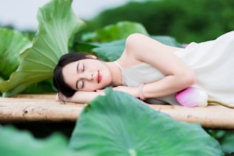 A woman peacefully rests on lotus leaves.