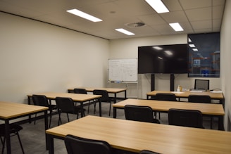A classroom with tables, chairs, and a large screen.