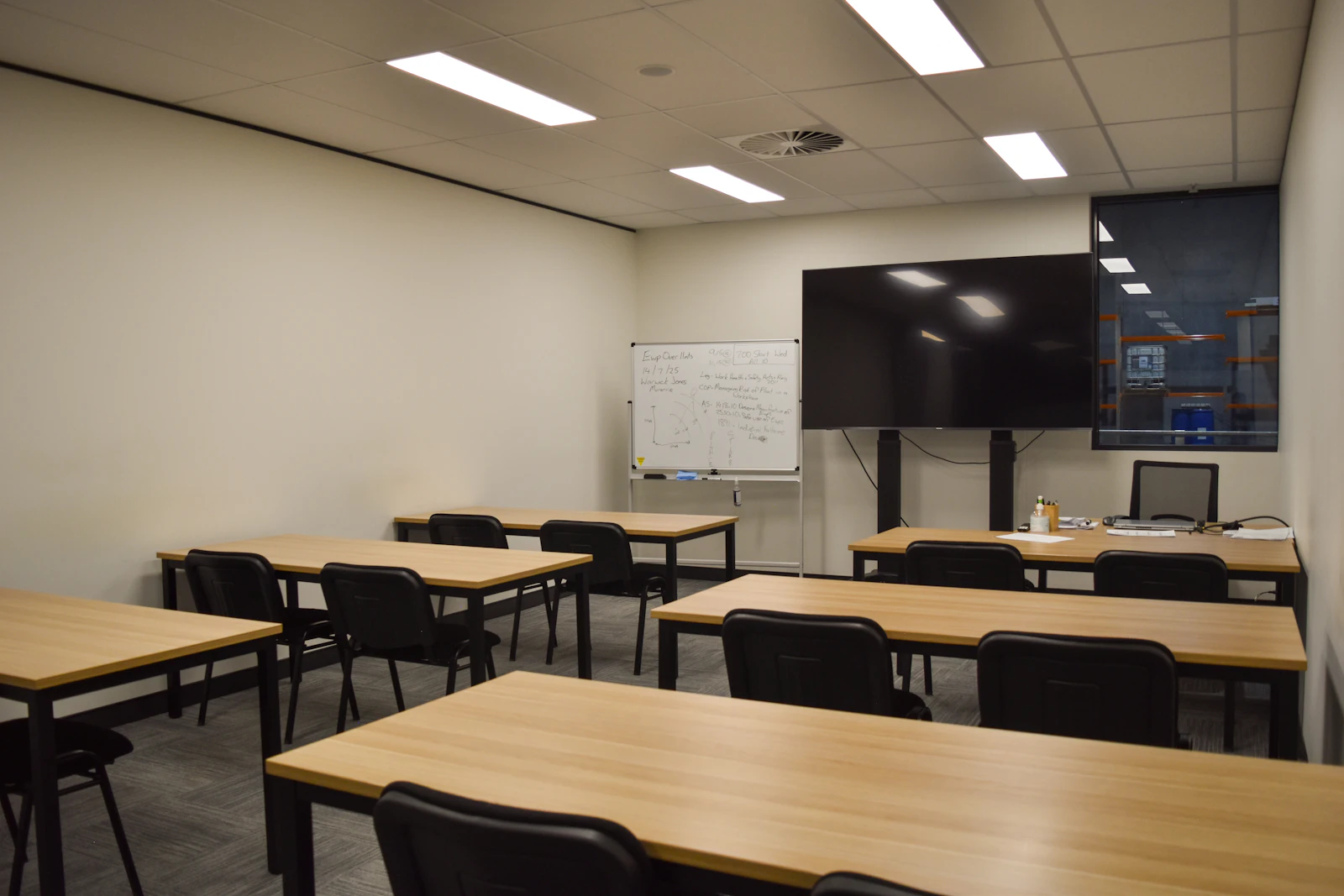 A classroom with tables, chairs, and a large screen