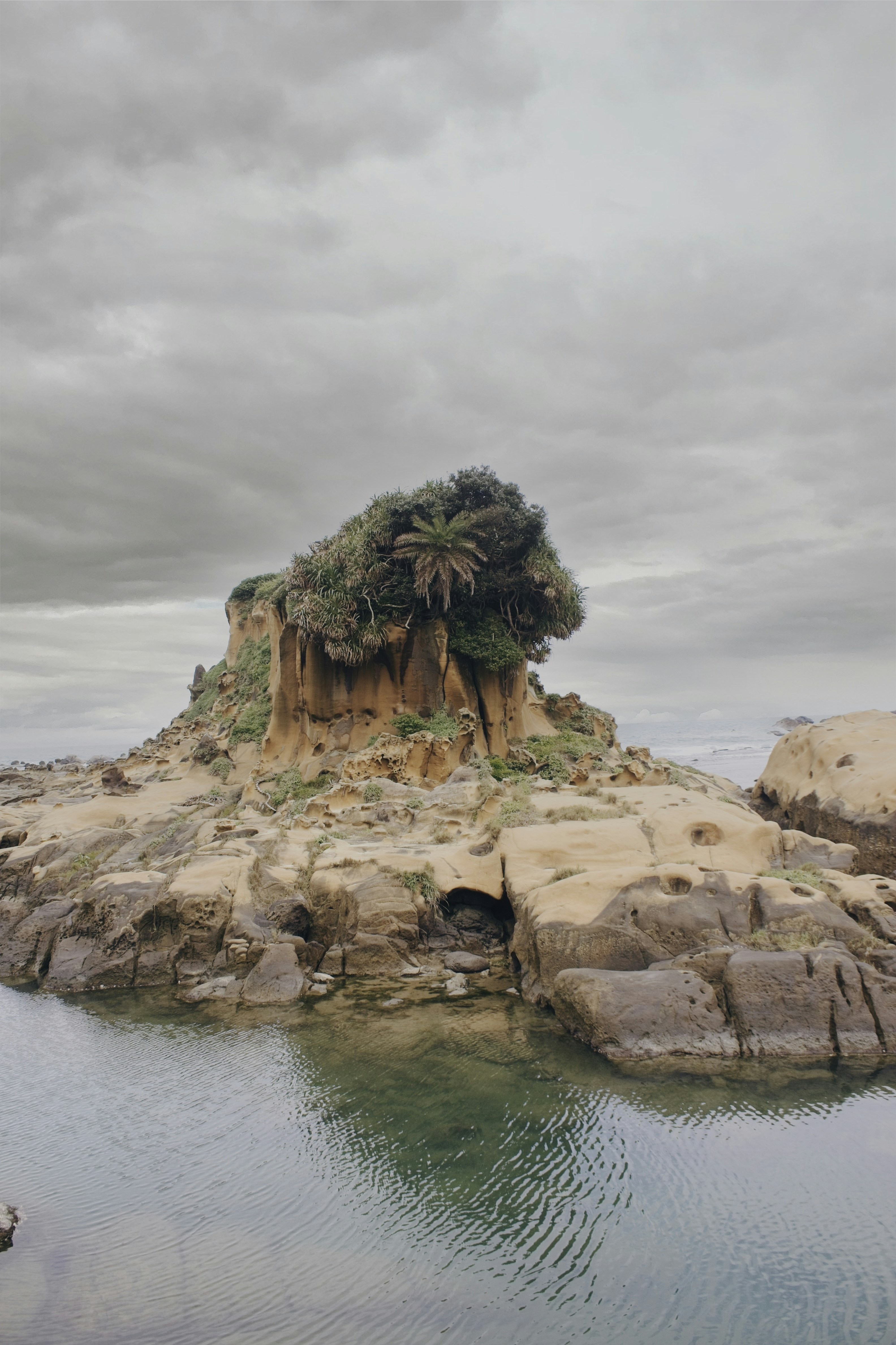 A rocky island stands beneath a cloudy sky.