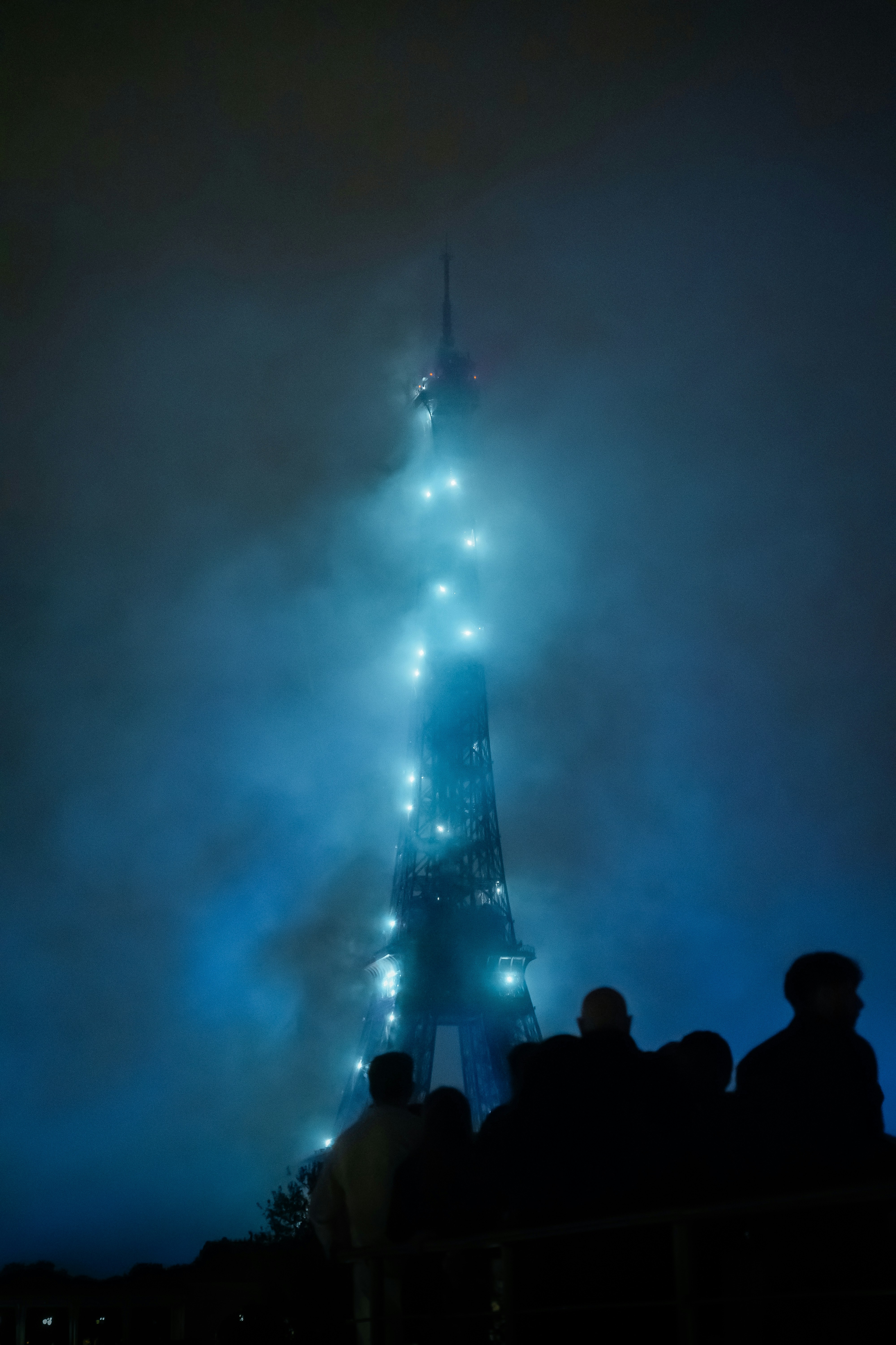 Eiffel tower lights shine in the foggy night sky.