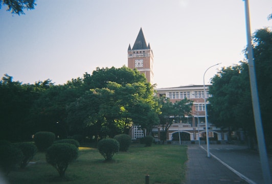 A clock tower looms over a lush green campus.